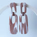 A pair of handmade rectangular drop earrings on a hanging white display arch.  The rectangular drop earrings have a cutout center, made from marbled polymer clay in shades of terracotta brown, shimmering copper, and white. The top and bottom segments are joined with antique copper-colored jump rings. The earrings have embedded titanium posts.