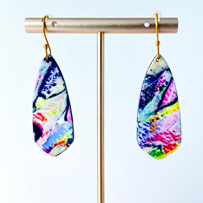 Asymmetrical dagger-shaped earrings made of polymer clay with vibrant brushstroke patterns in rainbow colors. Hanging on gold stainless steel earwires.