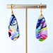 Asymmetrical dagger-shaped earrings made of polymer clay with vibrant brushstroke patterns in rainbow colors. Hanging on gold stainless steel earwires.