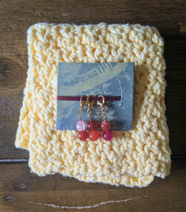 Photoraph of a set of three beaded stitch markers inspired by the sunset lesbian flag.