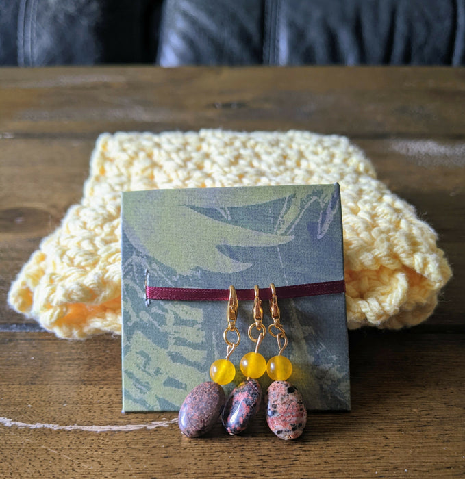Photograph of a set of three beaded stitch markers made with an brown, oblong rock bead and a small, round, yellow bead.