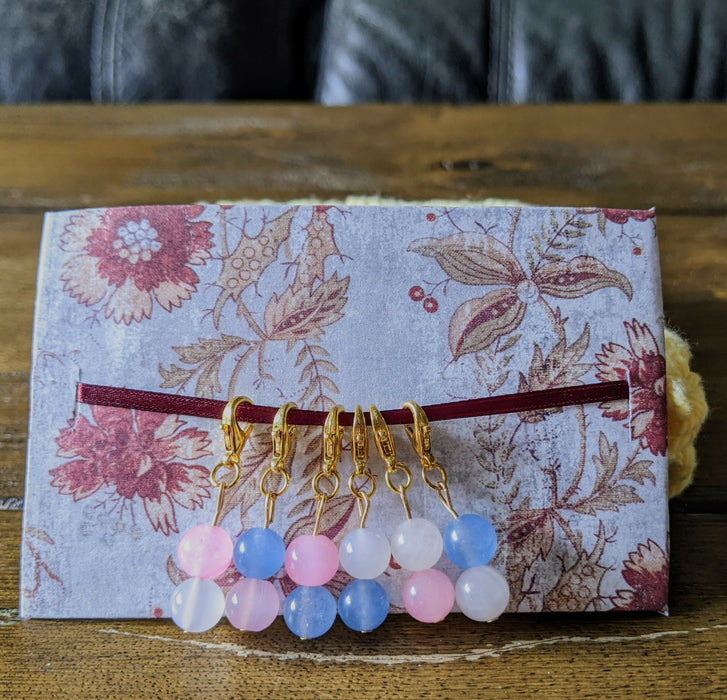 Photograph of a set of six beaded stitch markers inspired by the transgender flag.
