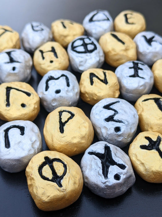 Close-up photograph of a set of Greek Alphabet Oracle stones painted in gold and silver.