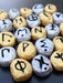 Close-up photograph of a set of Greek Alphabet Oracle stones painted in gold and silver.