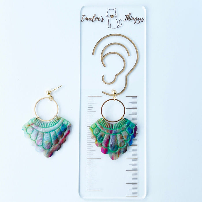 A pair of handmade fan-shaped polymer clay earrings displayed on a white background. The earrings feature gold-plated ball posts and hoops, with semi-transparent rainbow-colored clay and green etched fan-like lines. The marbling effect shows swirls of pink, blue, green, orange, and white.