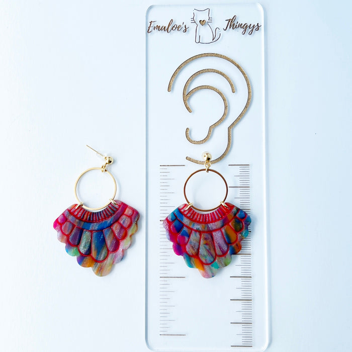 A pair of handmade fan-shaped polymer clay earrings displayed on a white background. The earrings feature gold-plated ball posts and hoops, with semi-transparent rainbow-colored clay and red etched fan-like lines. The marbling effect shows swirls of pink, blue, green, orange, and white.
