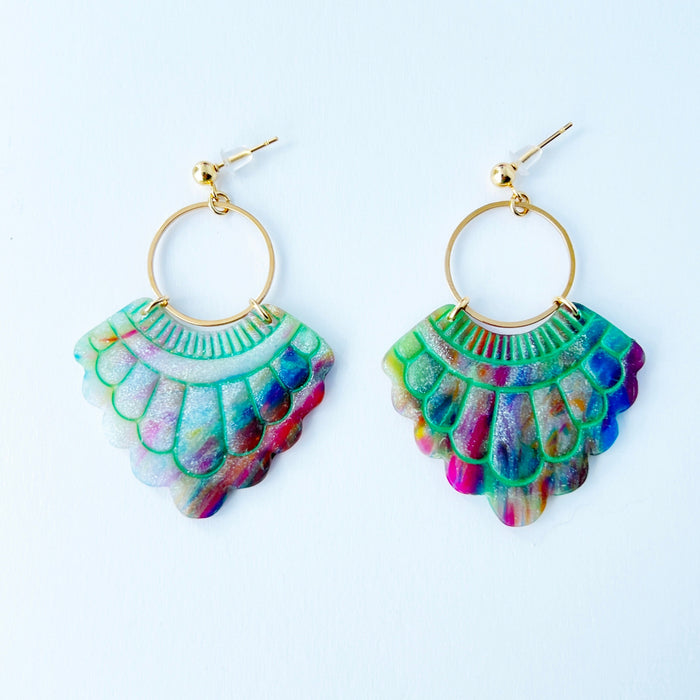 A pair of handmade fan-shaped polymer clay earrings displayed on a white background. The earrings feature gold-plated ball posts and hoops, with semi-transparent rainbow-colored clay and green etched fan-like lines. The marbling effect shows swirls of pink, blue, green, orange, and white.