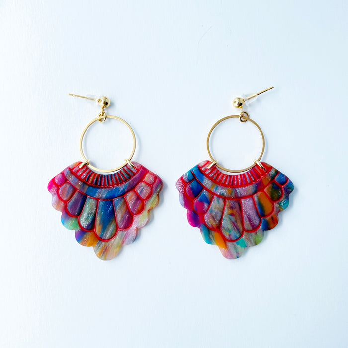 A pair of handmade fan-shaped polymer clay earrings displayed on a white background. The earrings feature gold-plated ball posts and hoops, with semi-transparent rainbow-colored clay and red etched fan-like lines. The marbling effect shows swirls of pink, blue, green, orange, and white.