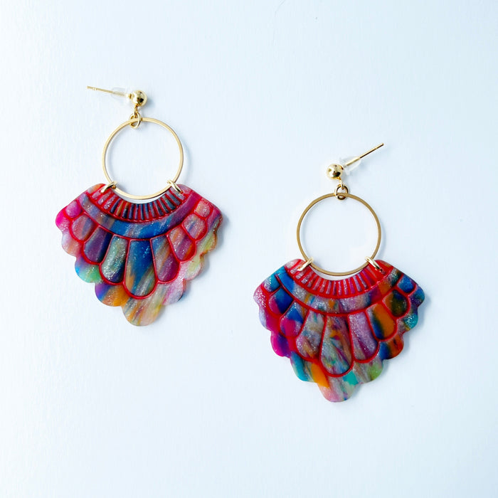 A pair of handmade fan-shaped polymer clay earrings displayed on a white background. The earrings feature gold-plated ball posts and hoops, with semi-transparent rainbow-colored clay and red etched fan-like lines. The marbling effect shows swirls of pink, blue, green, orange, and white.