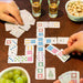 Colorful travel dominoes in the smaller domino size on a table with two people playing and snacks on a walnut wood table