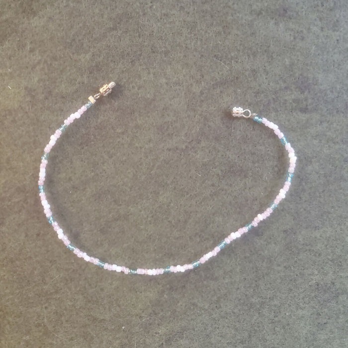 A bracelet with glass seed beads in light blue, pink, and white, arranged in a repeating pattern to look like the stripes of the trans pride flag