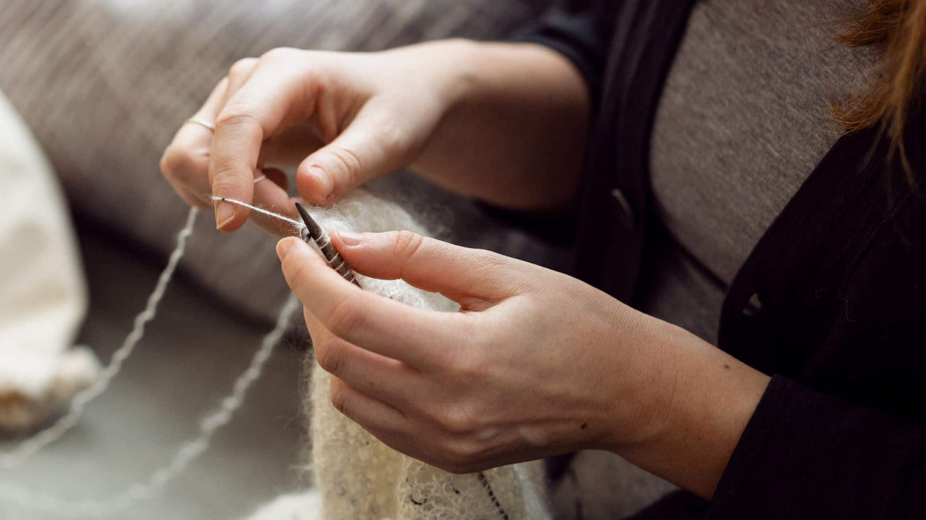 a person's hands knitting with white wool