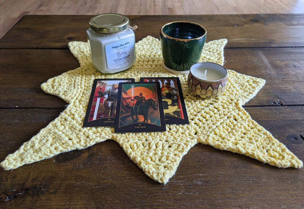 Photograph of the tarot cloth with two candles, a small ceramic cup, and a few tarot cards on it.
