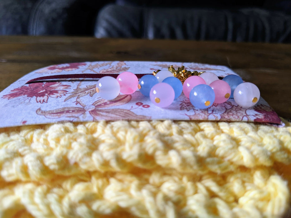 Photograph of the transgender flag stitch markers, taken from another angle.