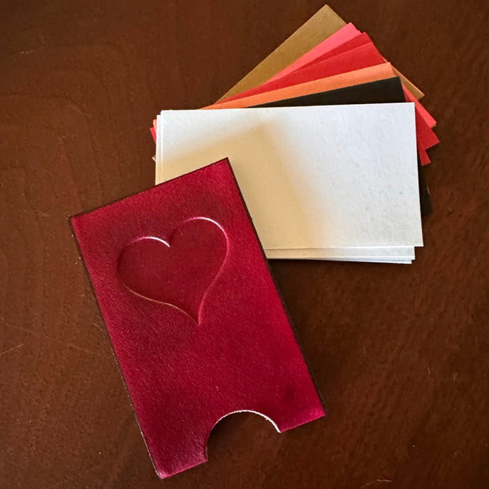 Red leather card case with heart debossed, and a small pile of blank love note cards, a on a walnut wood surface