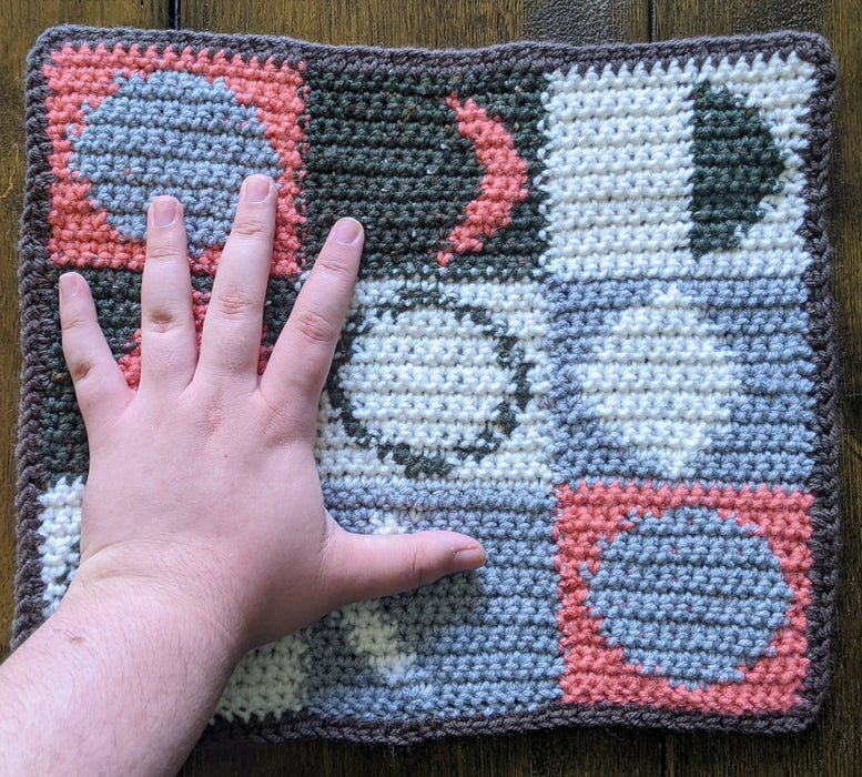 Photograph of the green, pink, and grey tarot cloth with the creator's hand on it for scale.
