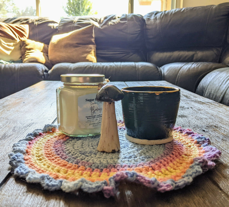 Photograph of a candle, a small ceramic cup, and a ceramic mushroom on the altar cloth.