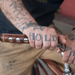 Tattooed man resting his hand on a bicycle city bar wrapped in a dark brown leather grip that has "porthole" round cutouts for finger holds. The man's hand tattoos say "HOLD FAST"