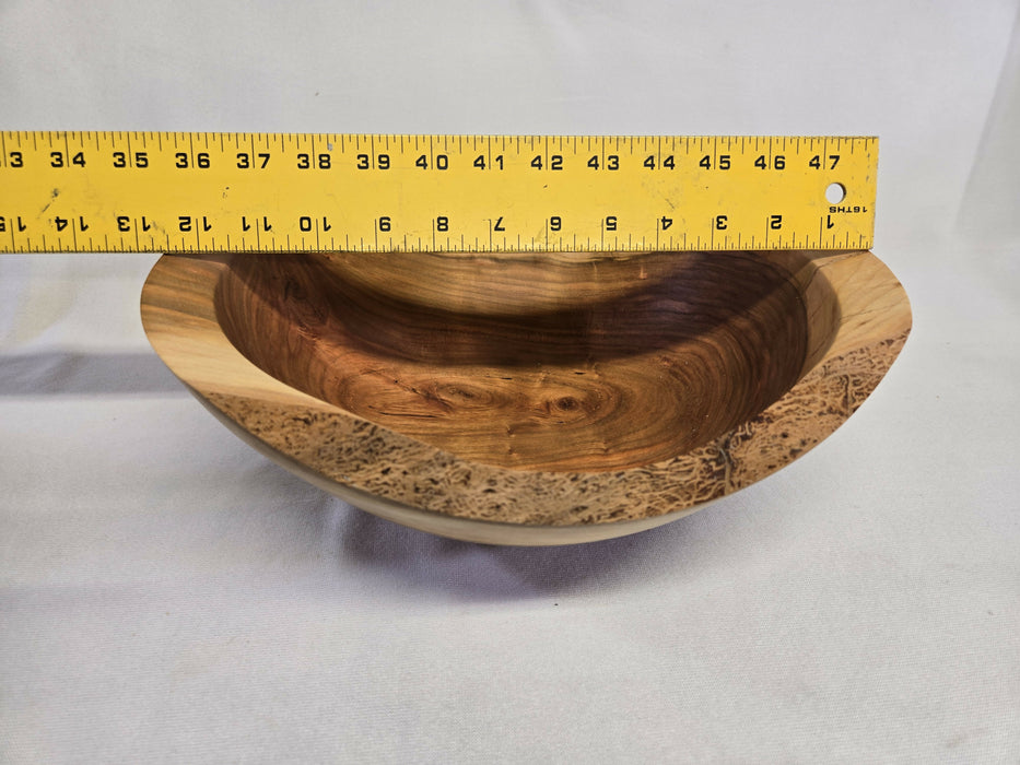 A picture of a wooden cherry bowl with a ruler on top measuring 12-1/2 inches