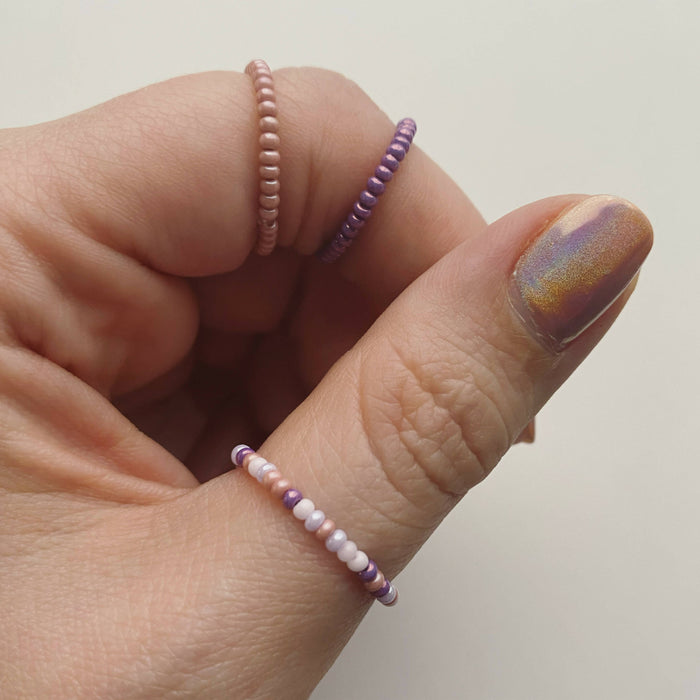 A woman's hand wearing three pink, purple and white beaded rings.