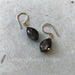 Two small earrings: glossy black marquise-cut stones, hung on gold hooks. One stone has an area of silver sheen that seems to be underneath the surface. Both stones are subtly microfaceted, a particularly rich and beautiful look.